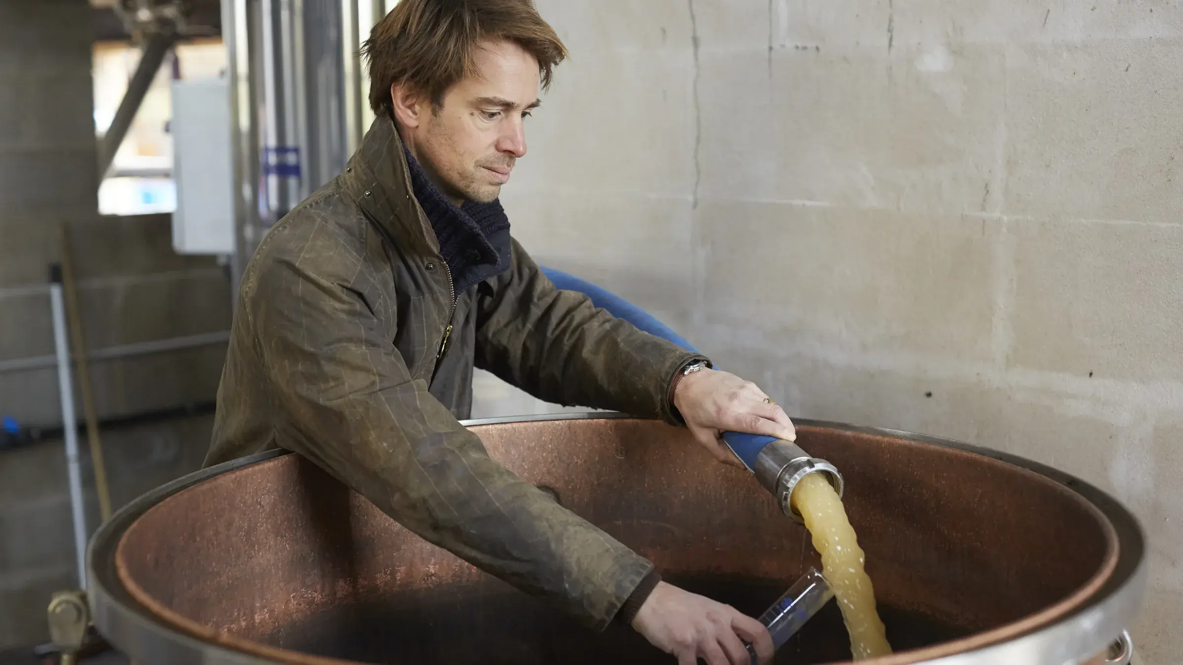 Étienne penché au-dessus de la cuve de brassage en cuivre, moût qui coule