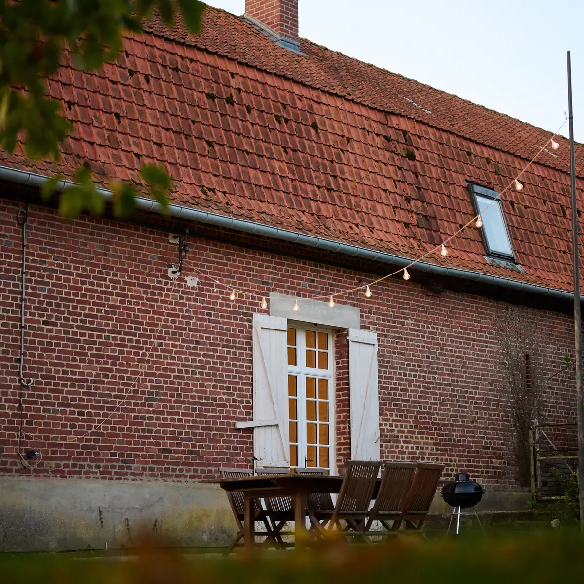 La porte vitrée du gîte sous sa guirlande d’ampoules, au pied de la façade de briques