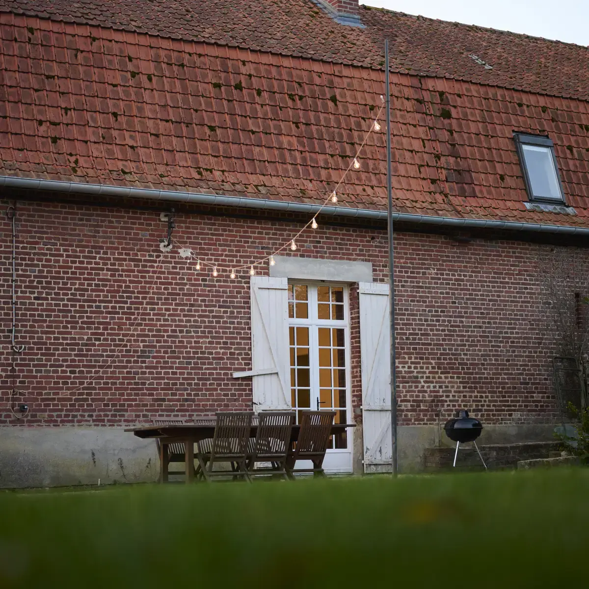 La façade en briques de la Maison de la Distillerie, sa porte vitrée et sa table de jardin