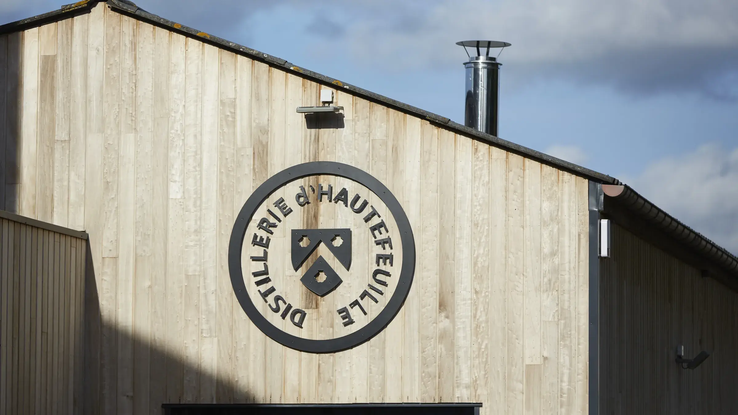 La façade en bardage de bois de la distillerie, marquée du sceau Distillerie d’Hautefeuille, sous un ciel d’été