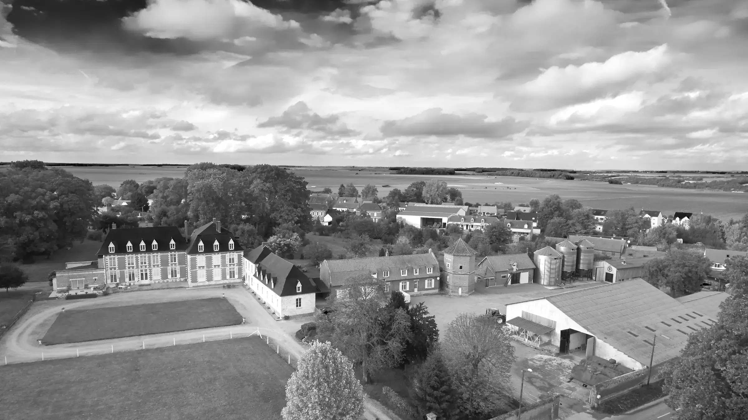 Vue aérienne en noir et blanc du château et de la ferme sous un ciel chargé